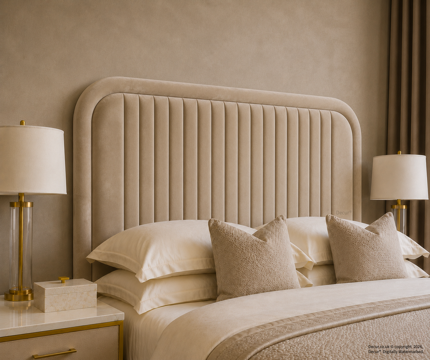 A luxury bedroom scene featuring a tall, vertically channel-tufted upholstered headboard in a warm beige/taupe velvet fabric, styled with cream bedding, textured beige accent pillows, and matching bedside tables with gold lamps.

Round Fluted Headboard